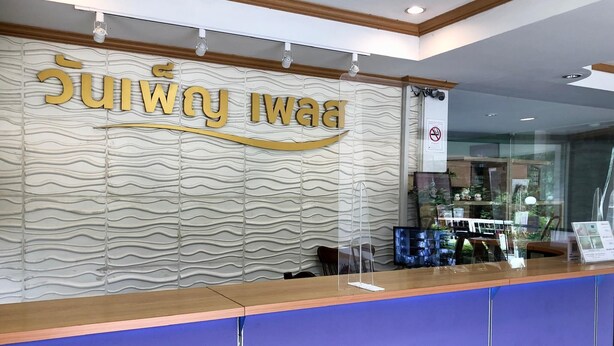 A reception desk with a wavy textured wall behind it, a clear glass barrier, and a no-smoking sign. - Wanpen Place (Udon Thani)