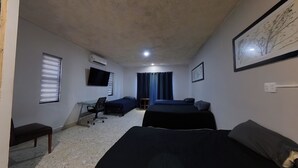 A room with two beds, a desk, a chair, a TV, and a window with blinds.