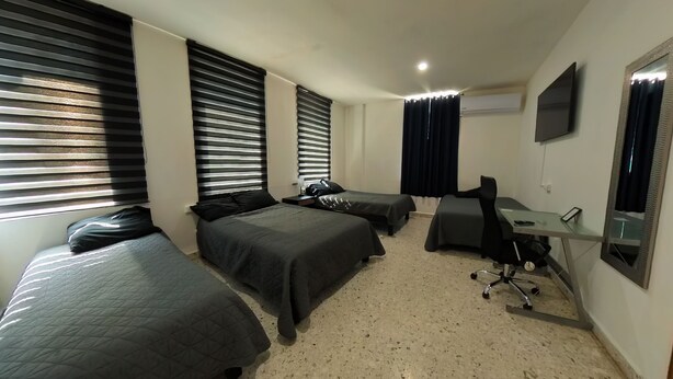 A hotel room with two single beds, a desk with a chair, a flat-screen TV, and a window with blinds.