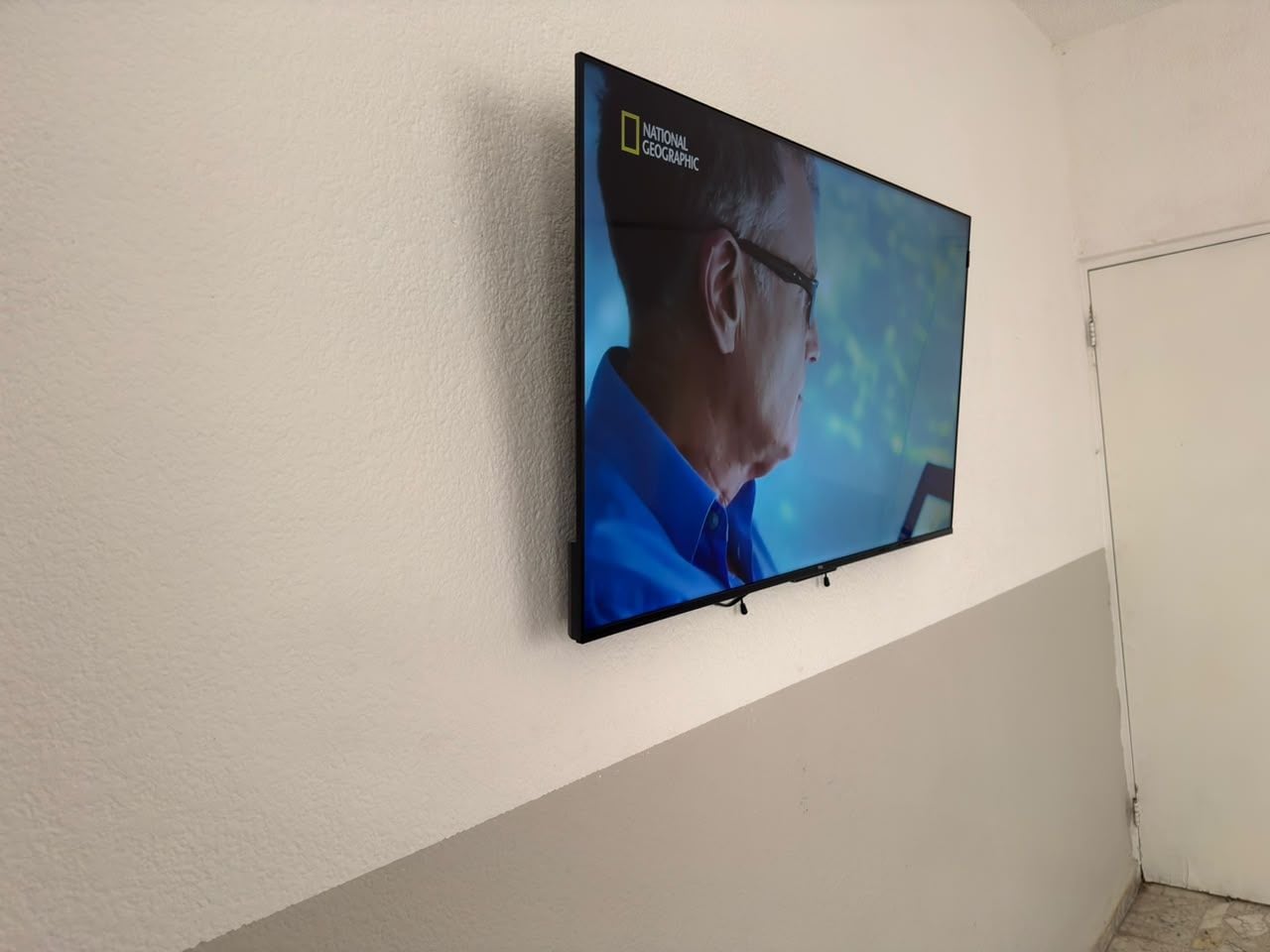 Een flatscreen televisie aan een muur, waarop een man in een blauw shirt te zien is.