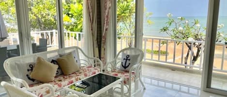 Un balcón con muebles de mimbre blanco, una mesa de vidrio y vista al mar.