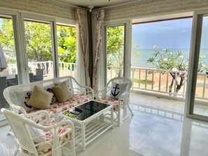 A balcony with white wicker furniture, a glass table, and a view of the sea. - Rim Chaam By Roomquest (Cha-am)