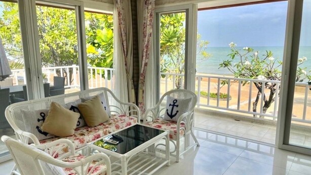 A balcony with white wicker furniture, a glass table, and a view of the sea. - Rim Chaam By Roomquest (Cha-am)
