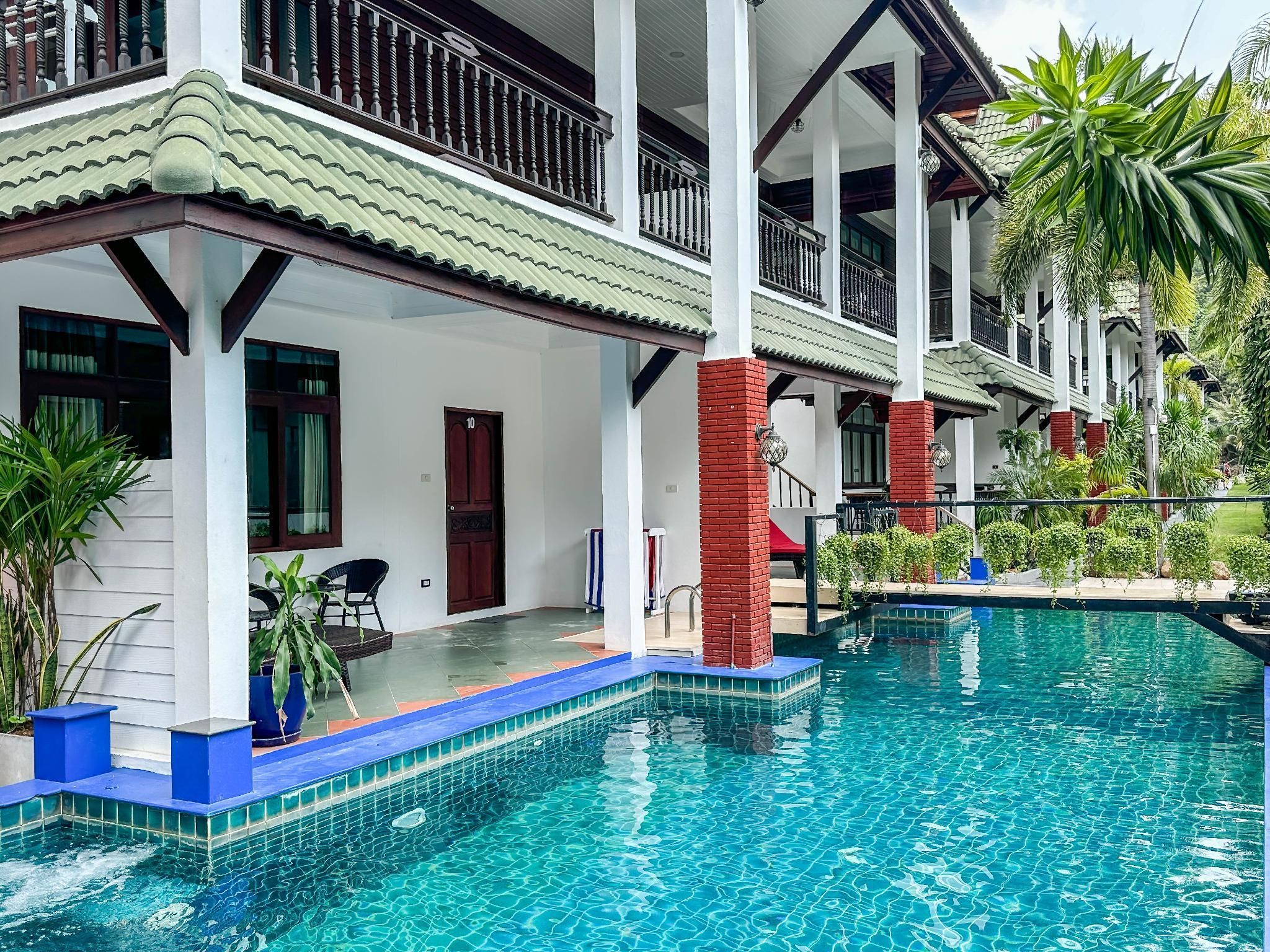 Un hotel con piscina, balcones cubiertos y abundante vegetación.