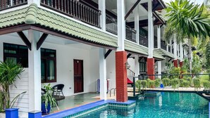 Un hotel con piscina, balcones cubiertos y abundante vegetación.