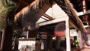 Zona de bar con techo de paja, suelo de baldosas y diferentes opciones de asientos.