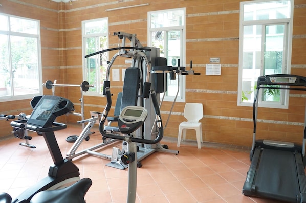 Ein Fitnessraum mit Trainingsgeräten, Laufband und weißem Stuhl.