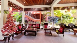 A covered outdoor seating area with wooden furniture, a Christmas tree, and a view of a building with a staircase. - Rainforest Huahin Hotel (Hua Hin)