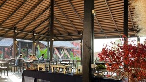 An outdoor dining area with tables and chairs, a covered roof, and a view of buildings in the background. - Rainforest Huahin Hotel (Hua Hin)