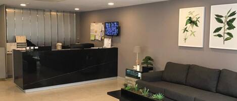 A reception area with a black reception desk, a flat-screen TV, a sofa, and two wall-mounted plant illustrations.