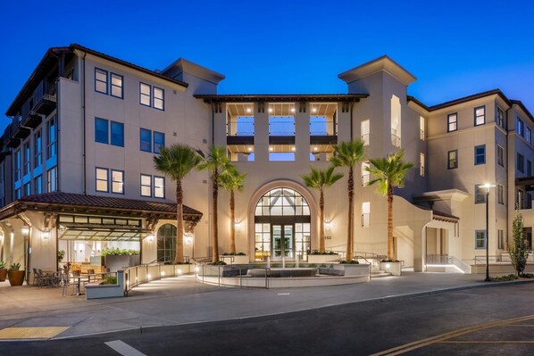 A multi-story hotel with a central entrance, palm trees, and a covered outdoor seating area. - Locale Menlo Park (Menlo Park)