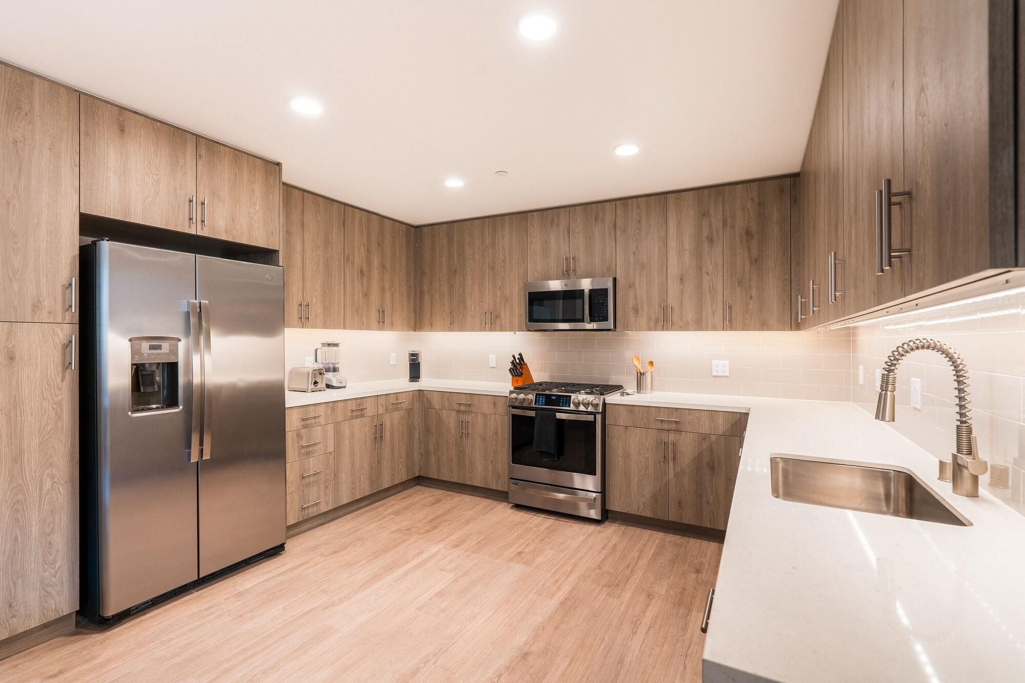 A modern kitchen with stainless steel appliances, wooden cabinets, and a white countertop.