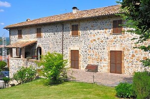 Un edificio de piedra con techo de tejas, una banca y un pequeño jardín.
