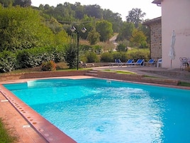 Una piscina con borde de ladrillo, rodeada de vegetación y un edificio con pared de piedra.