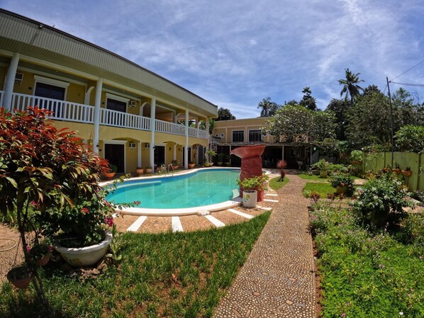 A two-story building with a swimming pool, surrounded by a garden with various plants and a paved walkway. - Hanbee S Resort (Puerto Princesa)