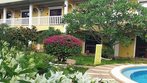 A hotel courtyard with a swimming pool, lush greenery, and a yellow building with balconies. - Hanbee S Resort (Puerto Princesa)