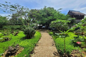 A garden pathway leading to a traditional thatched-roof building surrounded by lush greenery. - Hanbee S Resort (Puerto Princesa)