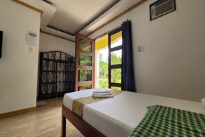 A single bed with a white mattress and a green checkered blanket, a wooden door with a metal grille, and a window with curtains. - Hanbee S Resort (Puerto Princesa)