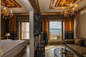 A hotel room with a bed, a sofa, a TV, a glass coffee table, and a view of the city. - By Mesut Resa Dence (Istanbul)