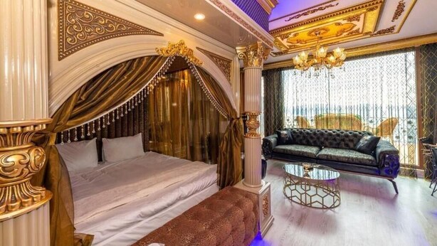 A luxurious bedroom with a large bed, a sofa, a chandelier, and ornate columns. - By Mesut Resa Dence (Istanbul)