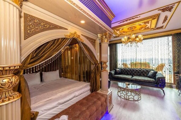 A luxurious bedroom with a large bed, a sofa, a chandelier, and ornate columns. - By Mesut Resa Dence (Istanbul)