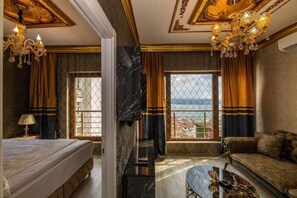 A hotel room with a bed, a sofa, a TV, a glass coffee table, and a view of the city. - By Mesut Resa Dence (Istanbul)