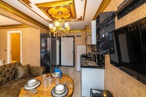A luxurious room with a dining area, a sofa, a chandelier, a kitchen, and a large TV. - By Mesut Resa Dence (Istanbul)