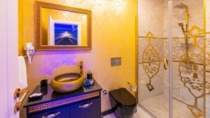 A bathroom with a marble wall, a large mirror with a decorative frame, a sink with a vessel basin, a toilet, and a shower with a patterned glass door. - By Mesut Resa Dence (Istanbul)