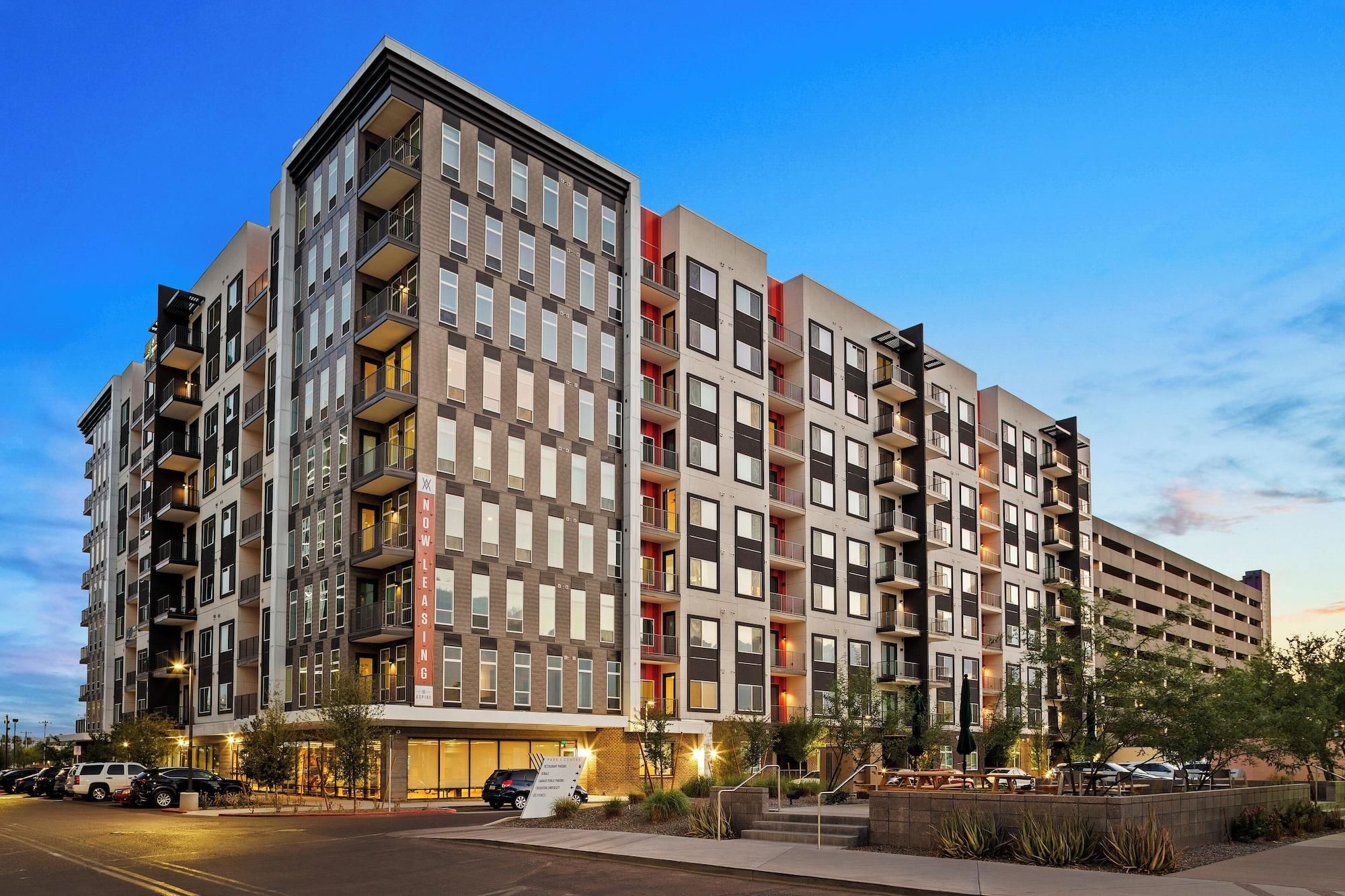 A multi-story hotel with a modern architectural design, featuring balconies and a parking area.