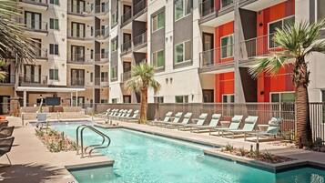A multi-story hotel with a swimming pool, outdoor seating, and palm trees.