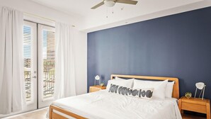 A bedroom with a bed, wooden headboard, white bedding, two bedside tables with lamps, and a view through a window with blinds. - Locale Midtown Phoenix (Phoenix)