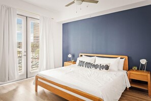 A bedroom with a bed, wooden headboard, white bedding, two bedside tables with lamps, and a view through a window with blinds. - Locale Midtown Phoenix (Phoenix)