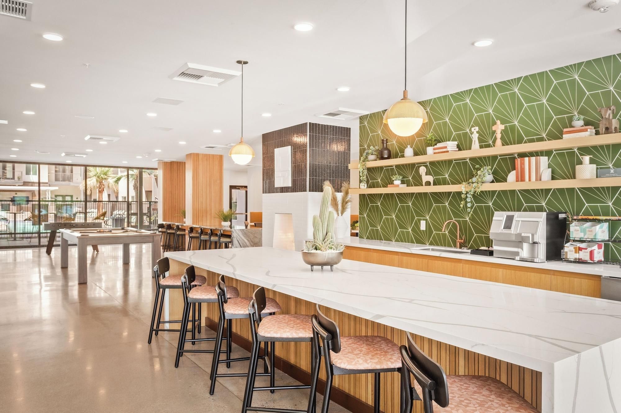 A modern bar area with a long counter, bar stools, and a green patterned wall.