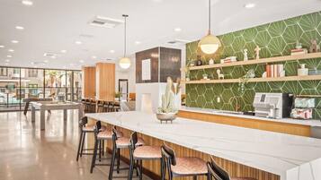 A modern bar area with a long counter, bar stools, and a green patterned wall.