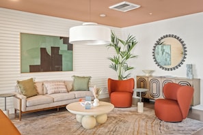 A modern living room with a sofa, armchairs, a coffee table, a large abstract painting, a potted plant, a mirror, and a decorative cabinet. - Locale Midtown Phoenix (Phoenix)