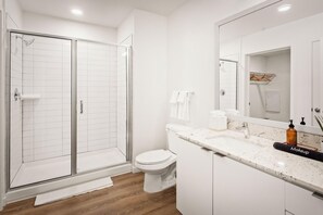 Une salle de bain moderne dotée d’une douche à parois de verre, de toilettes, d’un lavabo avec un plan de travail en marbre et d’un grand miroir.