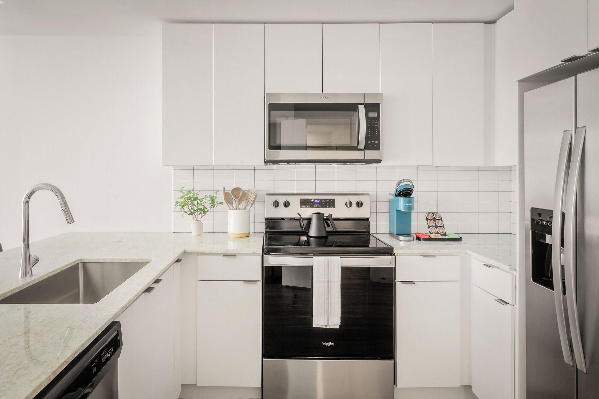 A modern kitchen with white cabinetry, a stainless steel microwave, a built-in oven, a dishwasher, and a refrigerator.