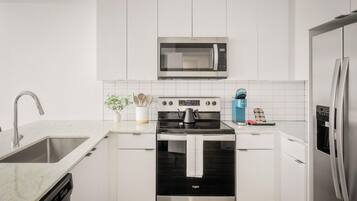 A modern kitchen with white cabinetry, a stainless steel microwave, a built-in oven, a dishwasher, and a refrigerator.