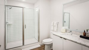 A modern bathroom with a glass-enclosed shower, a toilet, a sink with a mirror, and a countertop with a soap dispenser. - Locale Midtown Phoenix (Phoenix)