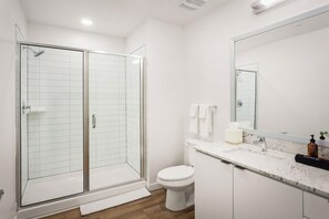 A modern bathroom with a glass-enclosed shower, a toilet, a sink with a mirror, and a countertop with a soap dispenser. - Locale Midtown Phoenix (Phoenix)