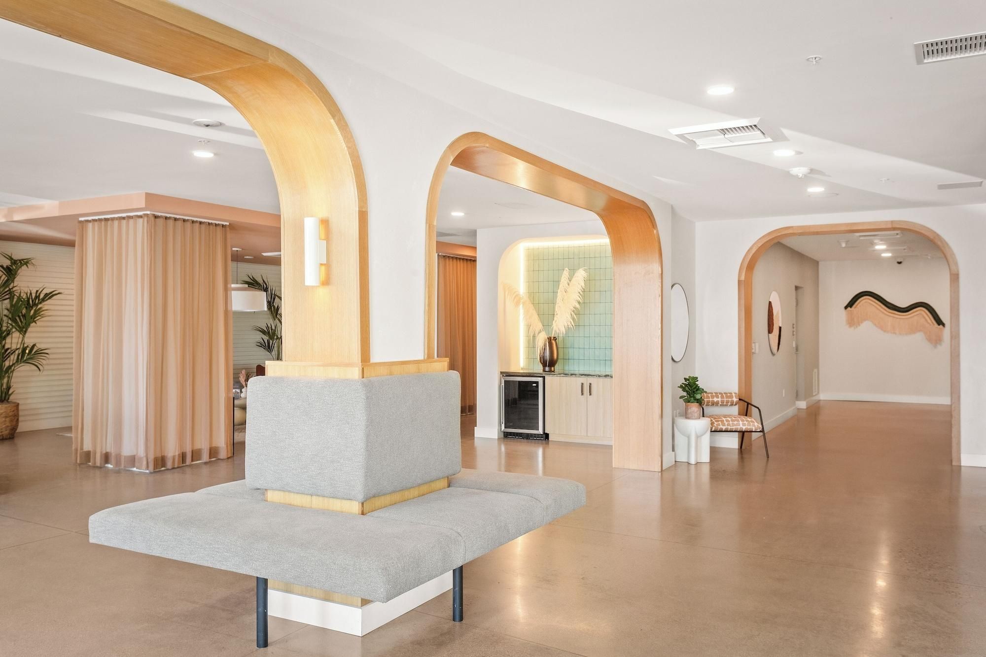 A spacious lobby with a modern design, featuring a grey sofa, wooden arches, and a kitchen area in the background.