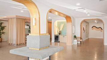 A spacious lobby with a modern design, featuring a grey sofa, wooden arches, and a kitchen area in the background.