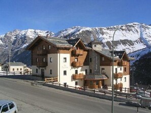 Un hotel de varios pisos con balcones, con montañas nevadas al fondo.