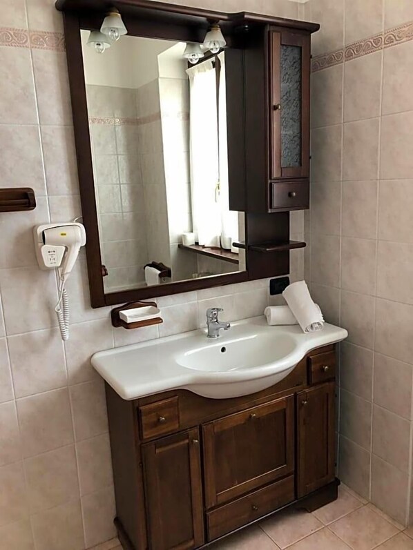 A bathroom with a white sink, a mirror, a telephone, and a wooden cabinet. - Hotel Adler (Menaggio)