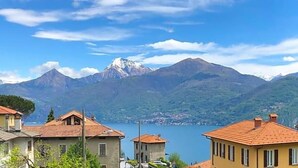 A mountain view with a lake, buildings with red roofs, and a sign for a hotel. - Hotel Adler (Menaggio)