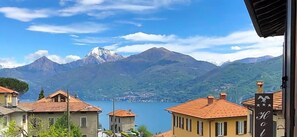 A mountain view with a lake, buildings with red roofs, and a sign for a hotel. - Hotel Adler (Menaggio)