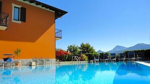 A clear swimming pool with lounge chairs and a building with a balcony. - Hotel Adler (Menaggio)