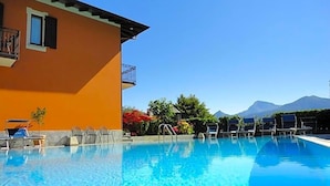 A clear swimming pool with lounge chairs and a building with a balcony. - Hotel Adler (Menaggio)