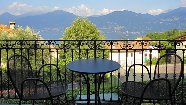 A balcony with a table and chairs, overlooking a mountainous landscape. - Hotel Adler (Menaggio)