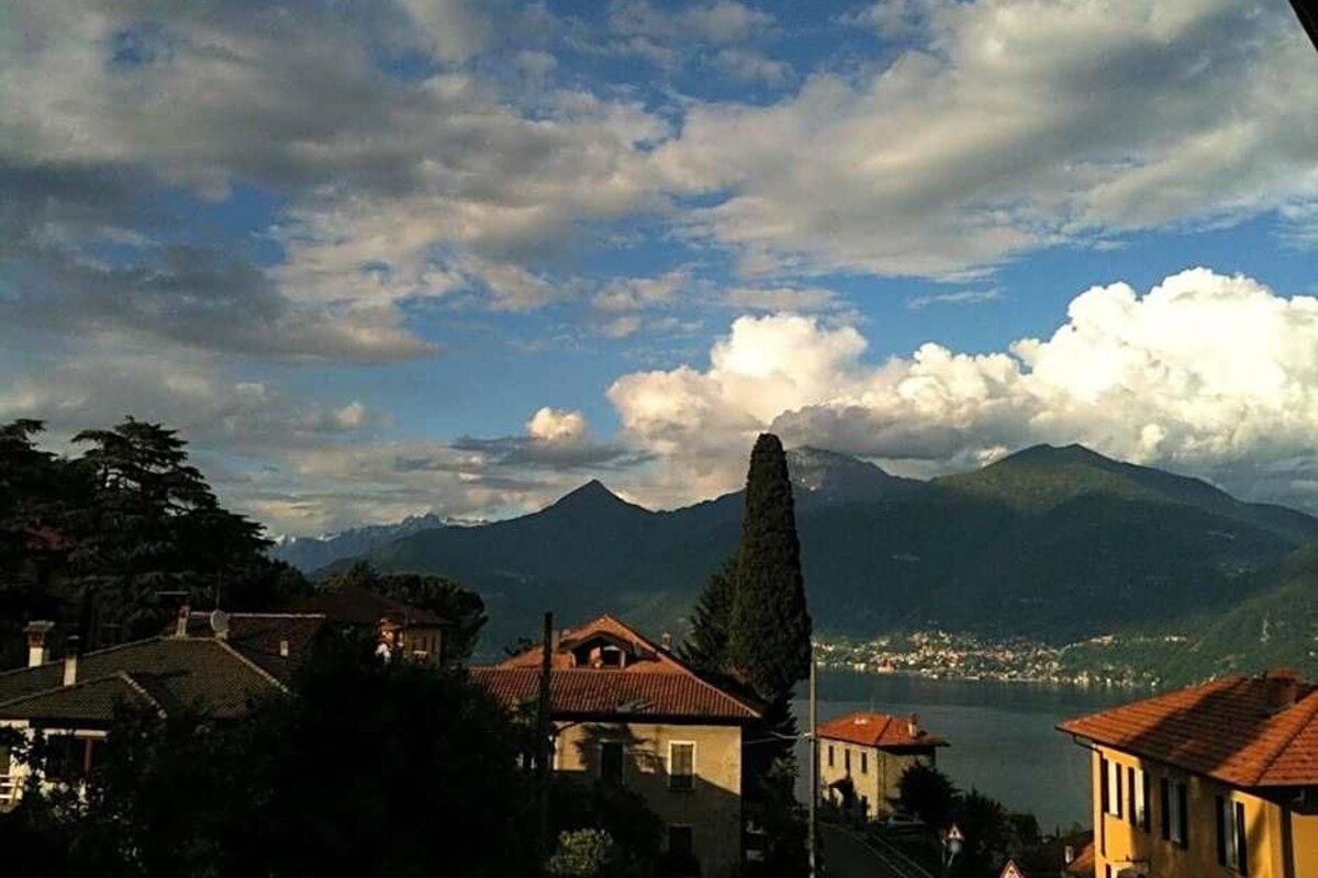 A mountainous landscape with a lake, houses with red roofs, and a clear sky with clouds.